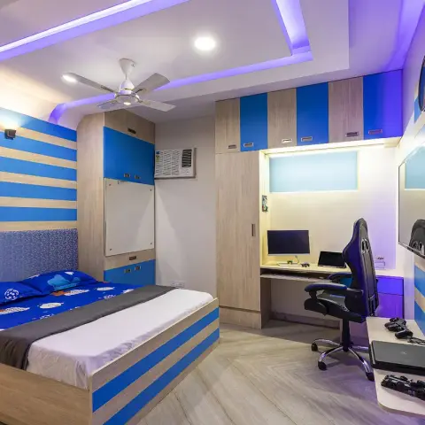 Blue-and-beige striped teen bedroom with a football-print bed, a built-in study desk with a gaming chair and monitor, a wall-mounted TV