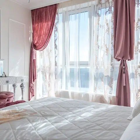 Blush bedroom against a corner window: dusty-rose velvet drapes with scroll-embroidered sheers and tasselled tie-backs