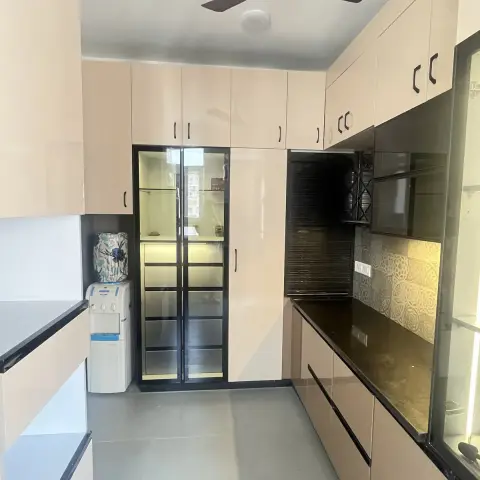 Blush-peach high-gloss L-kitchen with black C-channel handles and a black granite counter, grey-and-white patterned dado tiles lit by an under-cabinet strip