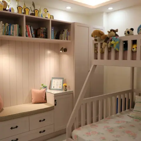 Blush-pink kids' room where soft toys line the guard rail of a custom bunk bed, facing a fluted-panel window seat with drawer storage under a trophy-topped