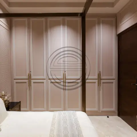 Blush-pink panelled wardrobe wall in a bedroom with a dark wood door and perforated jaali side panelling.