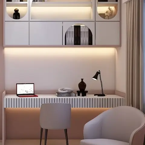 Blush-pink study nook with arched bookshelf niches lit from within, above a slatted built-in desk with a swivel lamp and grey accent chairs.