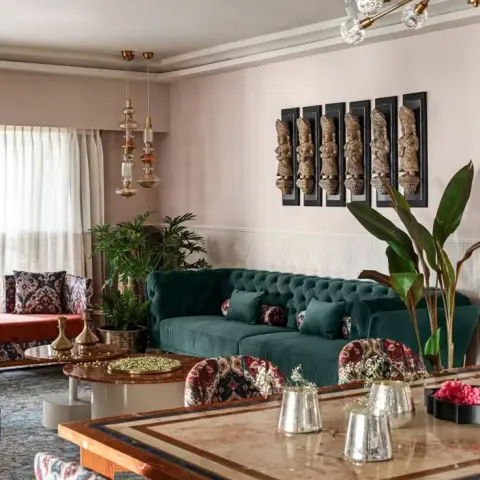 Blush-walled living room with an emerald velvet chesterfield under six carved wooden deity panels in black frames, a brass sputnik chandelier overhead