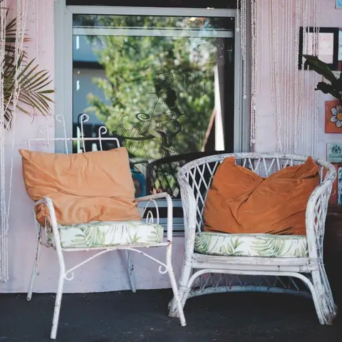 Boho home porch with a mismatched pair of weathered white wicker and metal chairs holding rust-orange cushions