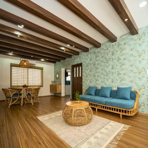 Boho living-dining space with a rattan sofa in teal cushions around a woven drum coffee table on a block-print rug, exposed wood beam ceiling