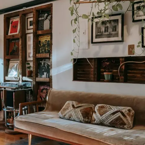 Boho living room corner with a vintage velvet sofa, geometric bolster pillows, a record-and-vinyl display shelf and a gallery wall framed by trailing pothos.