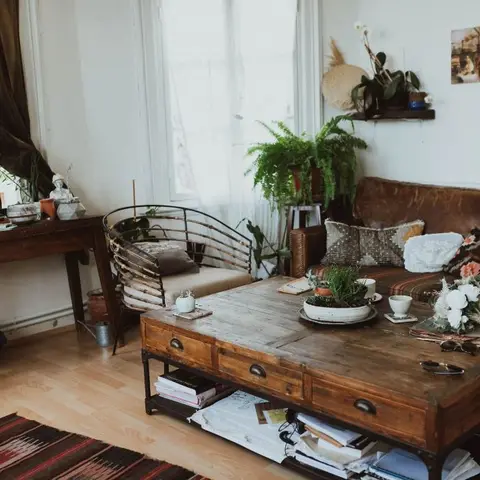 Boho living room with a brown leather sofa layered with kilim cushions, a wire-frame accent chair, and a chunky wooden trunk coffee table stacked with books