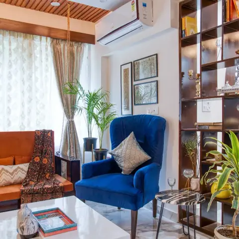 Boho living room with a hanging swing chair, a rust-orange sofa, a blue velvet wingback armchair and an open wood lattice-back bookshelf divider