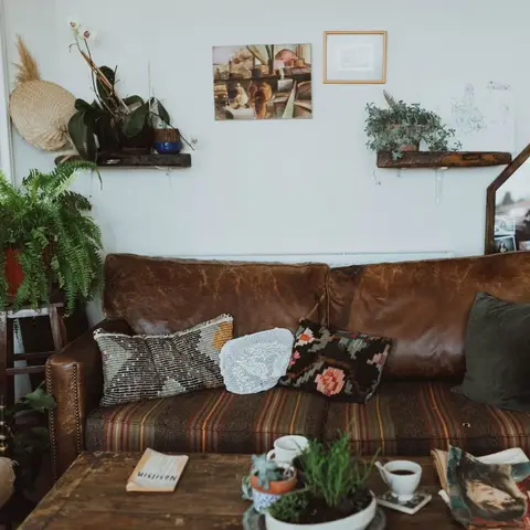 Boho living room with a worn brown leather sofa piled with patterned kilim and velvet cushions, layered gallery wall art