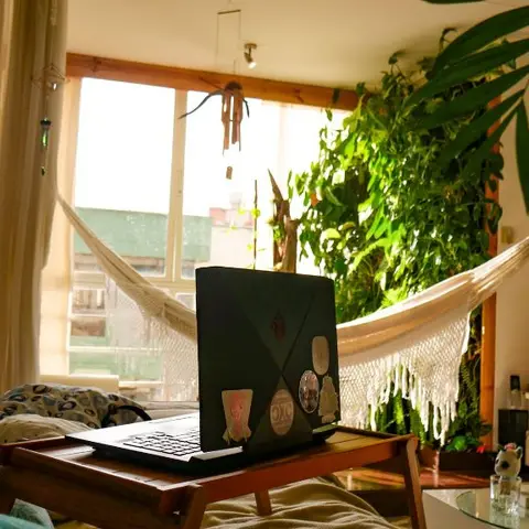 Boho living room with a woven macrame hammock chair and dense wall-mounted greenery beside a window, a small Buddha statue styled on a corner shelf