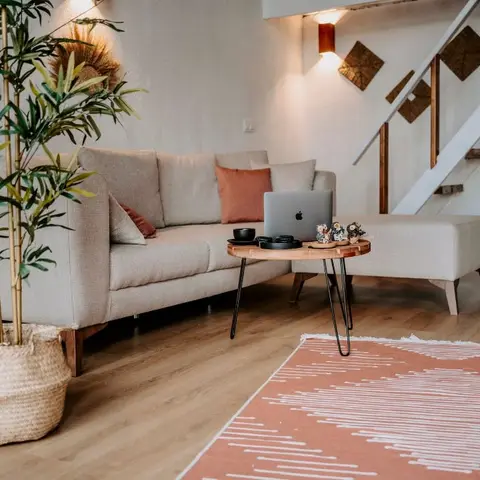 Boho-Scandinavian living room with a beige sectional sofa, a hairpin-leg coffee table and a terracotta patterned rug beneath an open wooden staircase.