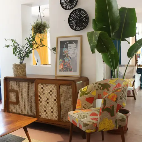 Boho-styled living room corner with a curved cane-front wood sideboard, a floral-print accent armchair, a large banana-leaf plant