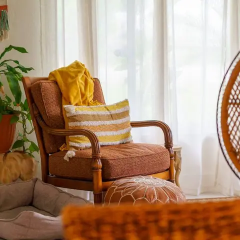 Boho-styled living room corner with a rattan-frame armchair, a mustard throw and striped cushion, a macrame wall hanging