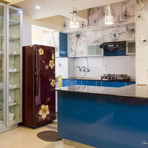 Bold blue modular kitchen with an island counter in black granite, a dandelion-print wallpaper backsplash wall, pendant lighting