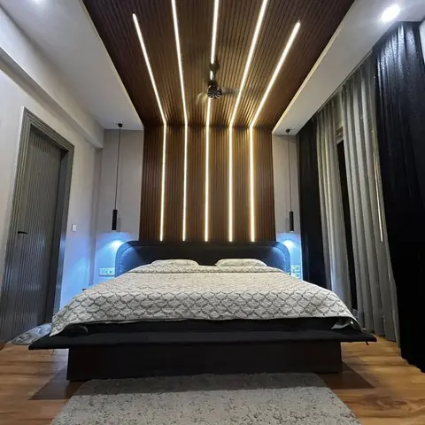 Bold master bedroom with a fluted wood-slat feature wall that wraps onto the ceiling, threaded with linear LED strips, over a dark upholstered platform bed.