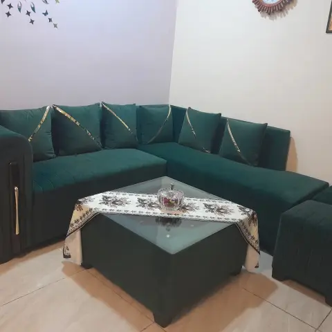Bottle-green channel-tufted corner sofa with gold-piped cushions sits around a matching upholstered coffee table with an inset glass top