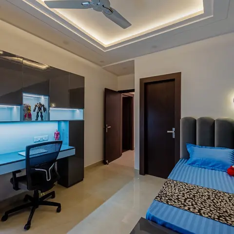 Boy's bedroom with a grey channel-tufted fluted headboard, a blue accent wall, a cove-lit ceiling, and a glossy backlit study unit with superhero figurines.