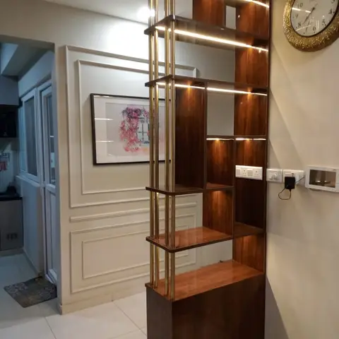Brass-framed wood display partition with accent lighting standing in an entrance foyer lined with cream wainscot wall panelling.