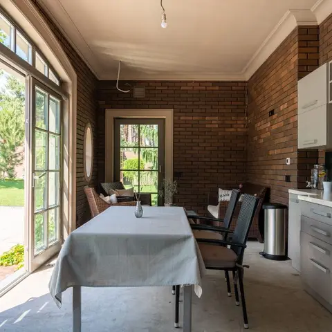 Brick-walled dining nook with a linen-covered table and dark metal chairs opening through arched glass doors onto a garden.