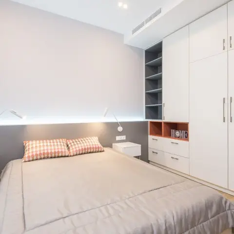 Bright bedroom with a grey upholstered headboard wall fitted with integrated reading lights, twin nightstands