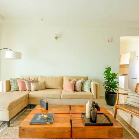Bright living room with a beige L-sectional dressed in blush and ikat cushions, a chunky mango-wood four-block coffee table on a jute rug, an arc floor lamp