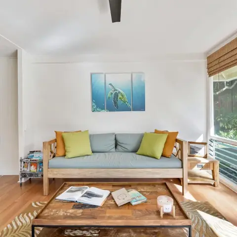 Bright living room with a teak-framed daybed sofa in grey-blue cushions under a three-panel sea-turtle canvas