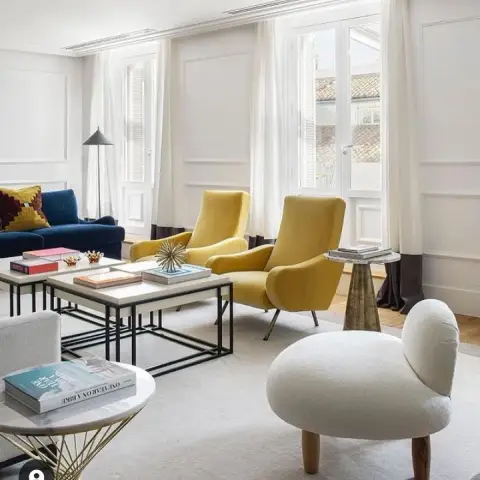Bright panelled living room with a pair of mustard velvet lounge chairs on brass legs set between two French windows, a navy sofa along the left wall