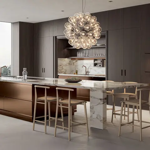 Bronze-fronted kitchen island with a book-matched marble waterfall countertop, topped by a cluster of glass bubble pendant lights