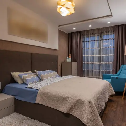 Brown button-tufted upholstered panel running the full bed wall, a folded white sculptural pendant overhead