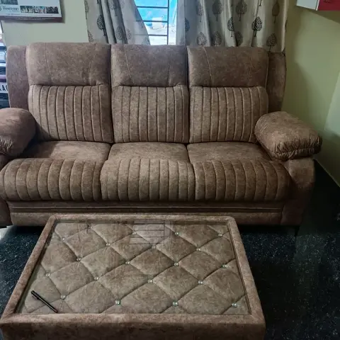 Brown channel-tufted three-seater sofa with a diamond-tufted glass-top coffee table on black granite flooring
