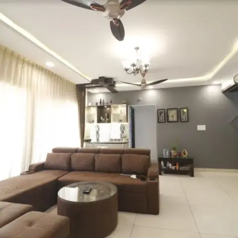 Brown fabric L-sofa with pull-out headrests and a round glass coffee table in front of a charcoal-grey accent wall hung with three small frames