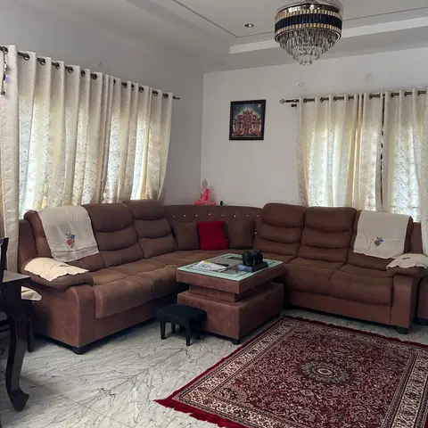 Brown sectional sofa with crocheted armrest covers around a two-tier coffee table, on a red Persian-style rug over polished marble flooring