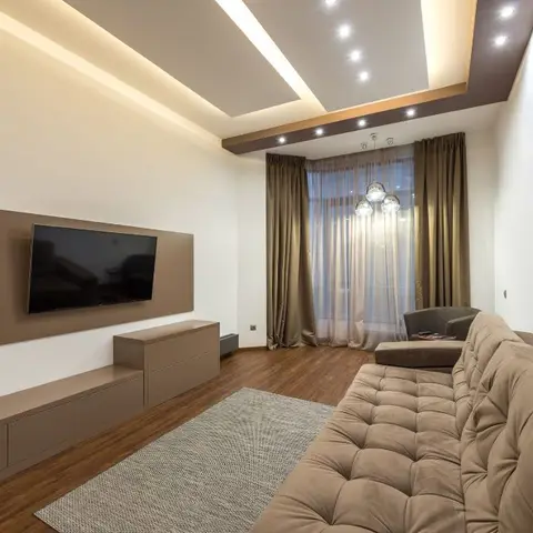 Brown-toned living room with a wall-mounted TV on a taupe panel above a long low floating console, tufted mink sofa