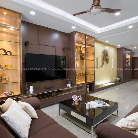 Brown-toned living room with a dark wood TV feature wall flanked by backlit glass display cabinets, a mustard textured accent wall