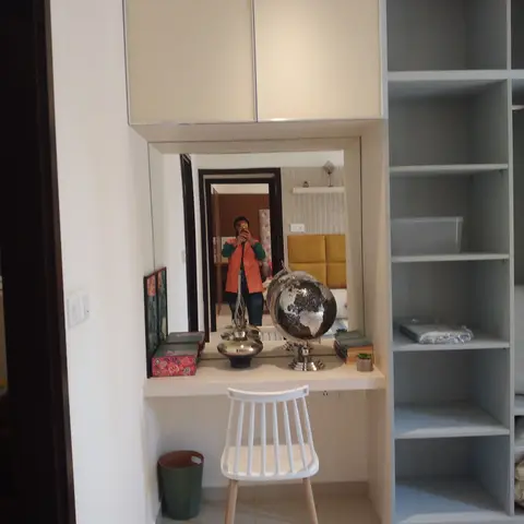 Built-in dressing nook with an overhead cabinet, a full-length mirror reflecting an adjoining bedroom, and an open wardrobe with shelving alongside.