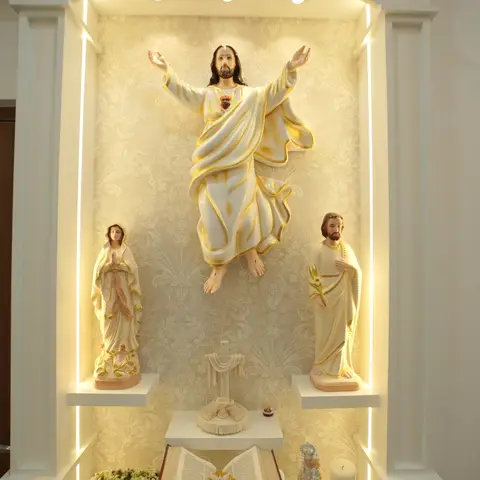 Built-in home prayer altar niche with an ornately moulded arch, back-lit gold wallpaper backdrop, and religious statues on a marble ledge.
