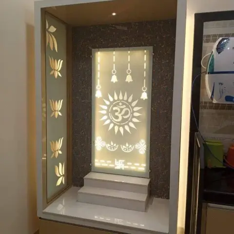 Built-in mandir niche with a backlit frosted panel etched with an Om sunburst, hanging bells and a swastika-marked rangoli border