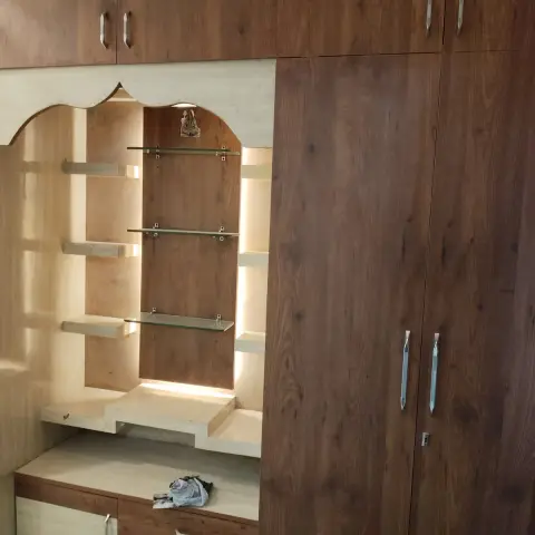 Built-in mandir with a scalloped cream arch framing a walnut back panel, three toughened glass shelves on clips