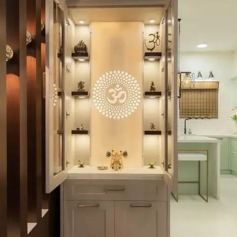 Built-in mandir with its glazed shaker doors folded back, brass idols standing on profile-lit dark wood ledges either side of a backlit lotus-Om motif