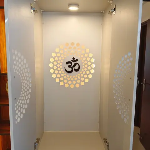 Built-in pooja cabinet with jaali-cutout doors opened to reveal a backlit Om medallion niche above a storage drawer.