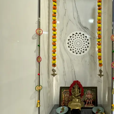 Built-in pooja niche lined in white grey-veined marble slab with a laser-cut circular mandala panel on the back wall