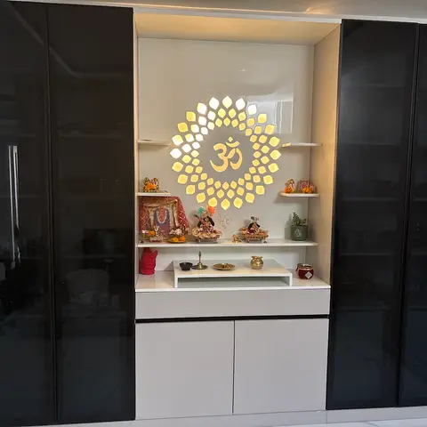 Built-in pooja unit with a backlit lotus-and-Om laser-cut panel and idols on floating shelves, flanked by black high-gloss wardrobes.