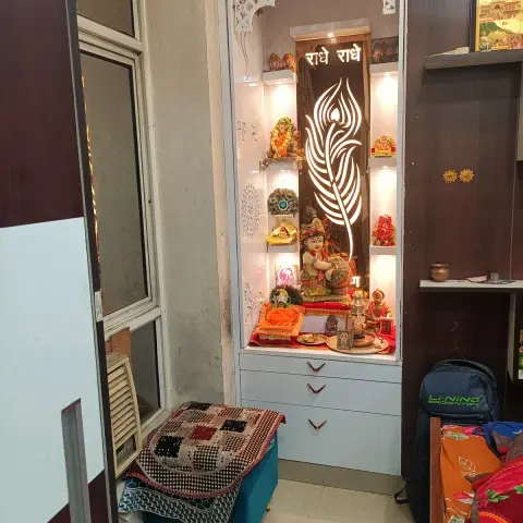 Built-in pooja unit with a backlit CNC-cut peacock-feather motif, a jaali arch overhang, illuminated idol shelves and drawer storage below.