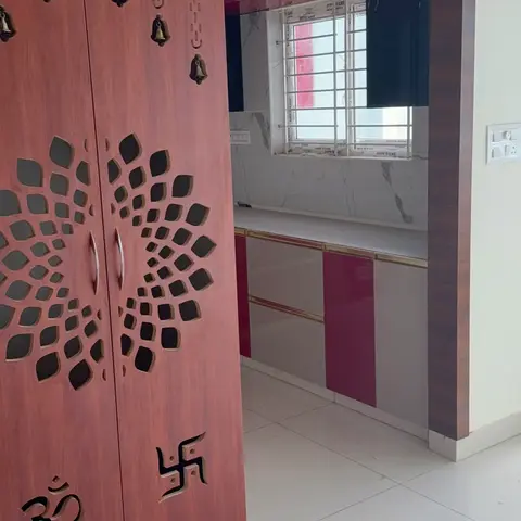 Built-in pooja unit with a CNC-cut mandala-pattern door inlaid with Om and swastika motif cutouts and hanging brass bells
