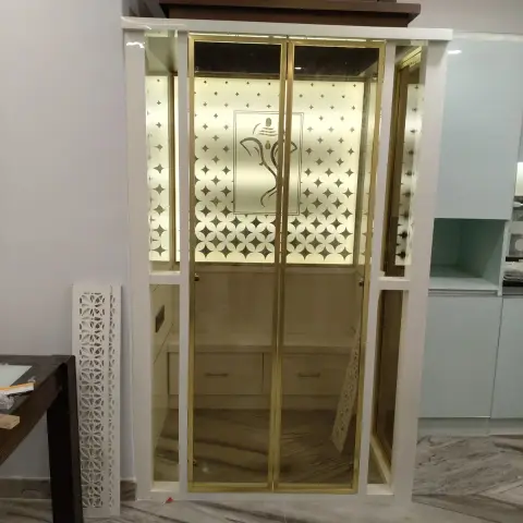 Built-in pooja unit with brass-framed etched glass doors featuring a backlit Ganesha motif, a peaked wood pediment above, and a jaali screen panel beside it.