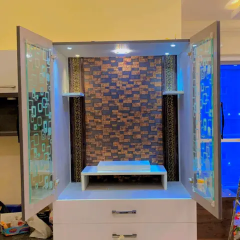 Built-in pooja unit with frosted glass doors, a backlit copper-toned mosaic stone accent wall, and LED strip lighting inside the niche.
