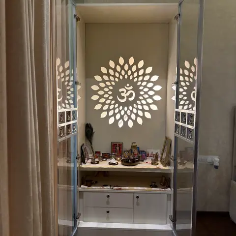 Built-in pooja unit with glass doors, brass temple bells on the door frames, a backlit lotus-and-Om wall motif