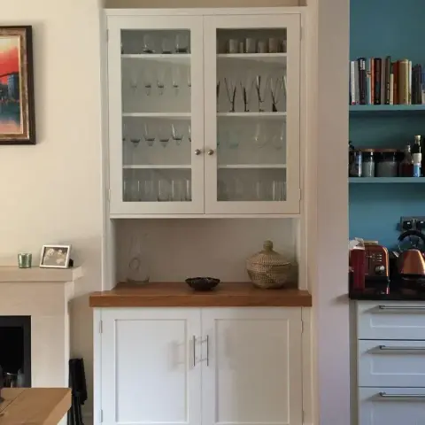 Built-in shaker crockery unit with glazed upper doors full of stemware and an oak counter, tucked in the alcove beside a limestone fireplace