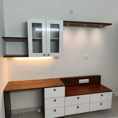 Built-in study desk and drawer unit in white and walnut-finish laminate, with a wall-mounted glass-front cabinet and a lit floating shelf above.