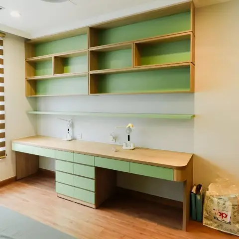 Built-in study desk for two with mint-green open shelving and drawer storage along a kids' bedroom wall, zebra blind at the window.